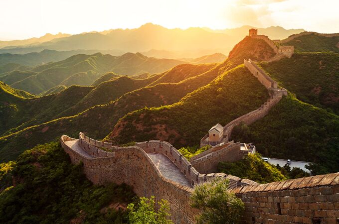 Die Große Mauer von China schlängelt sich durch eine malerische hügelige Landschaft im goldenen Licht der untergehenden Sonne. Dieses Bild symbolisiert Chinas reiche Geschichte und Kultur.