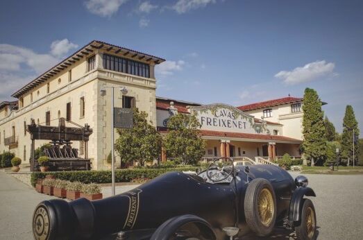 Historisches Freixenet-Gebäude in Spanien mit Oldtimer im Vordergrund und blauem Himmel im Hintergrund – Entdecken Sie die Welt des Premium-Cava!