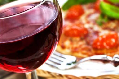 Ein Glas italienischer Rotwein vor einer Pizza mit Tomaten und Basilikum, perfekt für gesellige Abende.