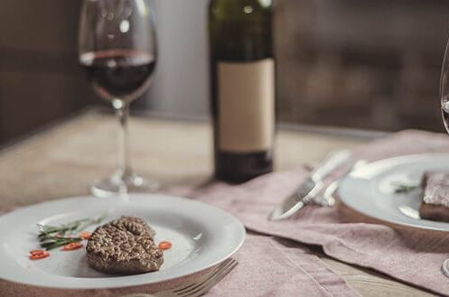 Zwei Gläser Merlot-Rotwein und zwei Teller mit Steak auf einem gedeckten Tisch, perfekt für ein elegantes Essen.