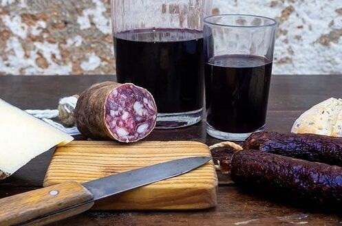 Spanischer Rotwein in Gläsern, serviert mit Hartkäse, Wurst und Brot auf einem rustikalen Holztisch – der perfekte Genussmoment!