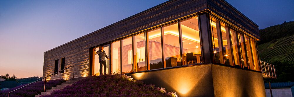 Das moderne Gebäude der Weingut Axel Pauly Vinothek bei Sonnenuntergang, umgeben von Lavendel und Weinbergen; idealer Ort für Weinprobe.