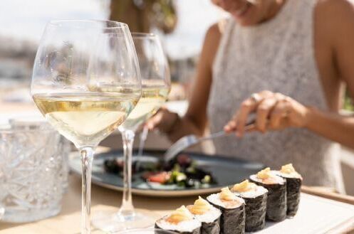 Zwei Gläser Weißwein mit Sushi-Teller im Freien serviert, ideal für Sushi-Mahlzeit im Sommer.