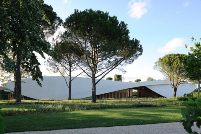 Moderner Cheval Blanc Weinkeller in Frankreich, umgeben von grünen Bäumen und gepflegten Rasenflächen, ideal für Weinliebhaber.