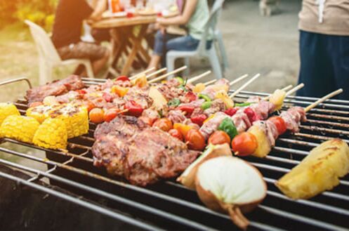 Verschiedene Grillspieße und Gemüse auf einem Grill im Garten, perfekte Begleitung für einen sommerlichen Grillabend mit Wein und Spirituosen.