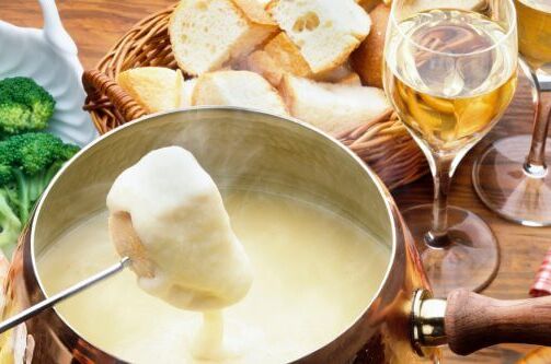 Käsefondue mit Brotwürfeln, frischen Garnelen und Brokkoli, serviert mit Weißwein im Glas. Perfekte Weinbegleitung für ein leckeres Fondue!