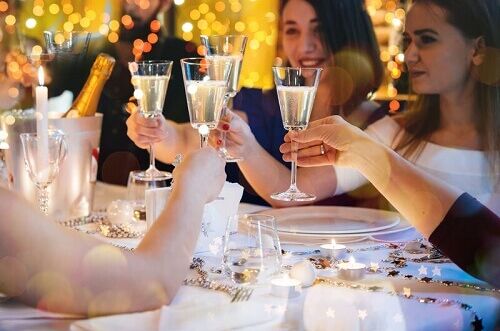 Fröhliche Gruppe feiert Weihnachten mit Sekt, stoßt mit Champagnergläsern an festlich gedecktem Tisch an, im Hintergrund Weihnachtslichter. Perfekt für festliche Anlässe!