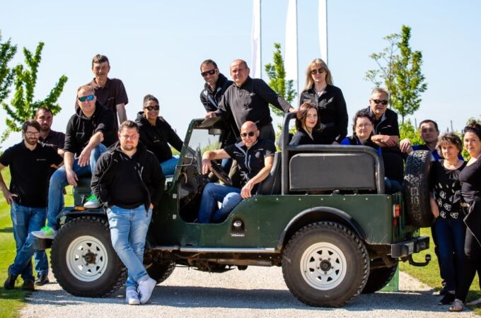 Das Team vom Weingut Studier posiert im Freien auf einem grünen Fahrzeug inmitten von Weinbergen unter blauem Himmel.