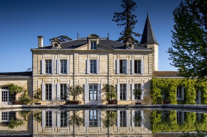 Das Château Cheval Blanc im Sonnenlicht, umgeben von Bäumen, klassisches Weingut in Frankreich, reflektiert in einem Teich. Ein Premium-Weingut!