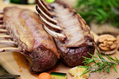 Nahaufnahme von gegrilltem Hirschfleisch auf Holzbrett mit Rosmarin, Gemüse und Glas Rotwein im Hintergrund. Perfekt für Wildgerichte!