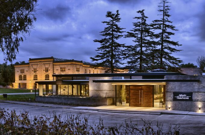 Historisches Gebäude der Bodegas Trapiche in Argentinien bei Dämmerung, umgeben von Bäumen und beleuchtetem Eingangsbereich, ein Symbol für exklusive Weine und Tradition.