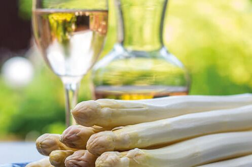 Stange weißer Spargel auf einem Teller, im Hintergrund ein Glas Weißwein und eine Flasche, perfekt zum Genuss von Spargelgerichten an einem sonnigen Tag.