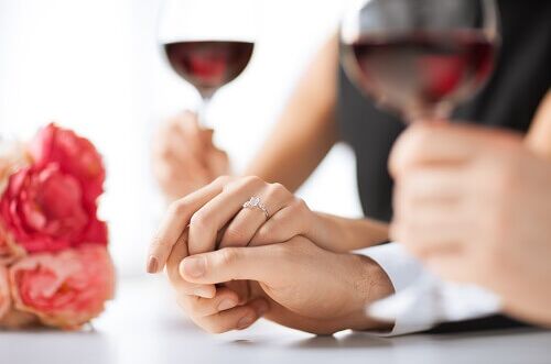 Ein Paar hält Hände bei einer Hochzeitsfeier mit Rotwein in der Hand, Rosen im Hintergrund. Ideal für romantische Anlässe.