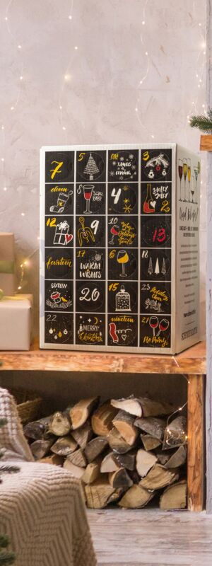 Wein Adventskalender in festlicher Atmosphäre in einem weihnachtlich dekorierten Raum. Im Vordergrund steht ein Wein-Adventskalender mit 24 nummerierten Türchen, die weihnachtliche Symbole und Schriftzüge zeigen.