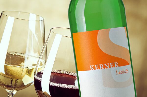 Grüne Flasche Schneekloth Lieblich-Wein vor zwei gefüllten Weingläsern, eines mit Weißwein und eines mit Rotwein. Genussvoller Weinmoment.