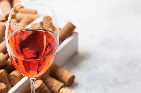 Ein Glas Roséwein gefüllt mit pinkroter Flüssigkeit, auf einem Tisch mit Korken im Hintergrund. Perfekt für Sommerabende genießen!