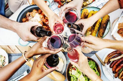 Grillparty mit Freunden, die Rotwein aus Weingläsern genießen; saftige Würste und frisches Gemüse im Hintergrund. Ideal für gesellige Sommerabende!