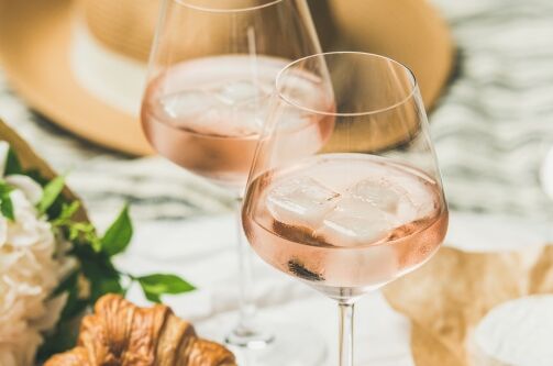 Zwei Gläser gekühlter Roséwein mit Eiswürfeln, arrangiert mit Blumen und Käse auf einem Picknicktisch. Perfekt für einen erfrischenden Sommergenuss!