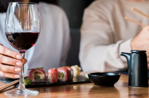 Nahaufnahme von Personen, die an einem Tisch Rotwein trinken und Sushi essen. Perfekte Kombination aus edlem Rotwein und frischem Sushi.