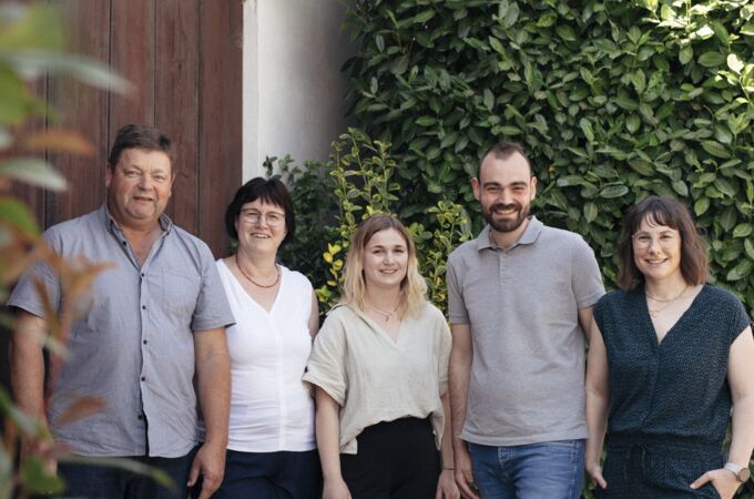 Die Familie Noll vor dem Weingut, umgeben von Weinreben. Entdecken Sie die Leidenschaft für Wein aus Deutschland!