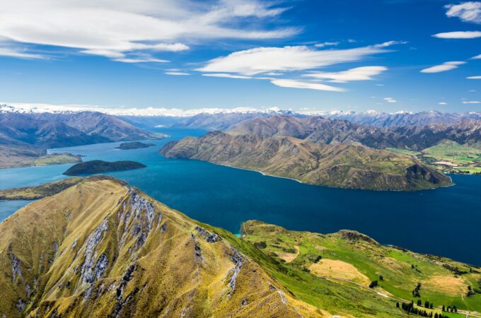 Luftaufnahme einer Landschaft in Neuseeland: Klare blaue Seen, grüne Hügel und schroffe Berge, die sich bis zum Horizont erstrecken.