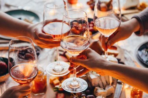 Gruppe von Menschen stößt mit Gläsern Roséwein an, umgeben von Käse und Früchten auf einem gedeckten Tisch, ideal für gesellige Bio-Wein-Momente.