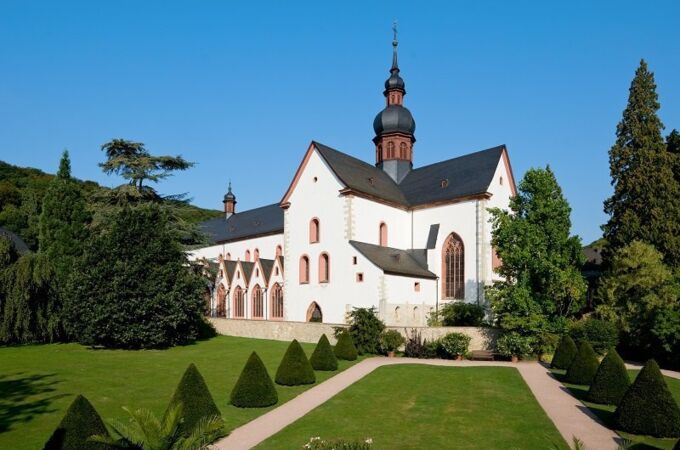 Kloster Eberbach in Hessen mit gepflegter Gartenanlage und gotischem Gebäudeteil vor blauem Himmel. Historisches Weingut und Kloster.