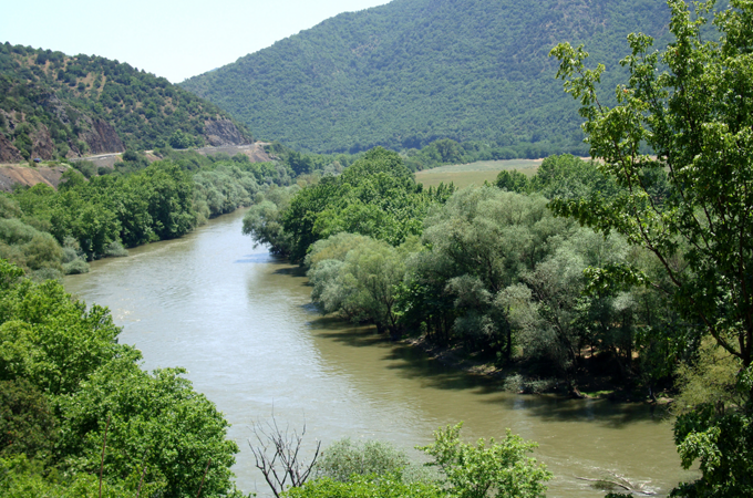 Ein Fluss schlängelt sich durch eine üppig grüne Landschaft in Nordmazedonien, umgeben von bewaldeten Hügeln.