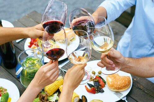 Menschen stoßen mit verschiedenen Sommerweinen bei einem festlichen Essen im Freien an. Perfekt für sonnige Tage!