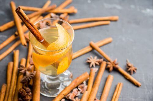 Glas hellen Weißweins als Glühwein mit Zimtstangen und Zitrusschalen auf grauem Hintergrund. Genießen Sie winterlichen Genuss mit hinzugefügtem Zimt.