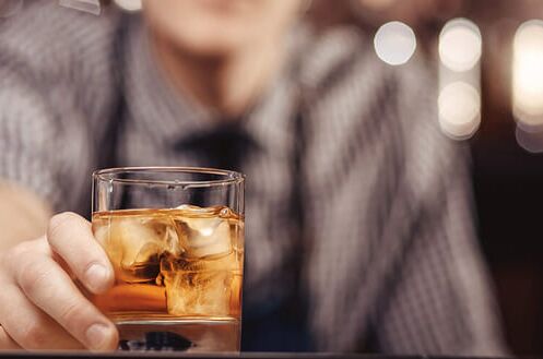 Mann hält ein Glas amerikanischen Whiskey mit Eiswürfeln in einer Bar vor sich. Genießen Sie hochwertigen US-Whiskey.