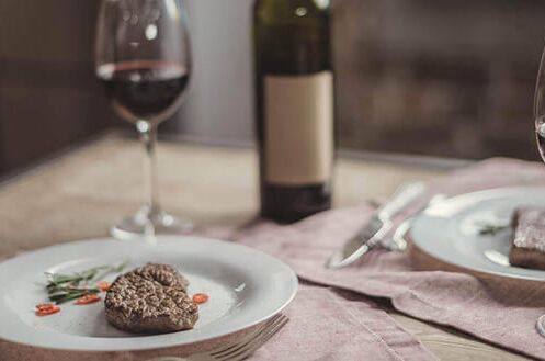 Zwei Weingläser mit Rotwein und Teller mit Steak und Gemüse auf einem Tisch mit rosa Tischläufern