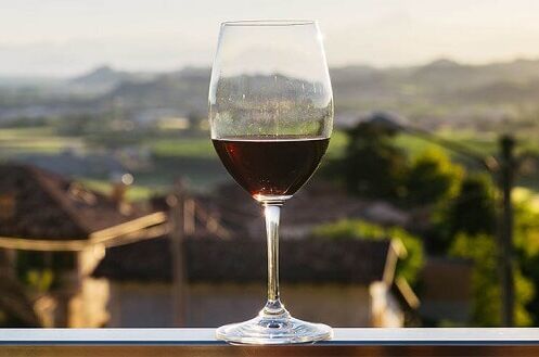 Ein Glas italienischer Rotwein auf einem Balkon, mit Blick auf eine malerische Hügellandschaft im Hintergrund. Genießen Sie den Geschmack Italiens!