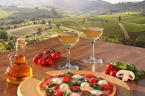 Zwei Gläser italienischer Weißwein und eine Pizza auf einem Holztisch in ländlicher italienischer Landschaft. Genießen Sie italienisches Lebensgefühl!