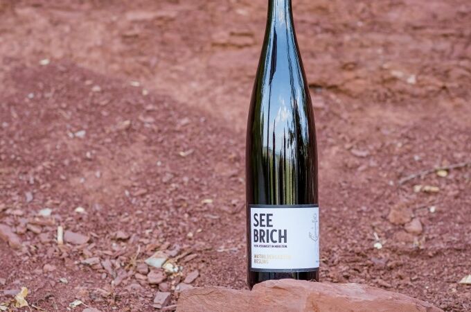 Flasche Seebrich Riesling Wein auf rotem Boden liegend im Freien. Weingut Seebrich, Deutschland. Perfekt für Weinliebhaber!