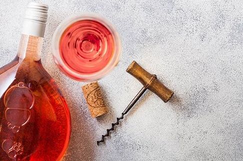 Flasche französischer Roséwein und gefülltes Weinglas mit Korkenzieher und Korken auf grauem Hintergrund, perfekte Begleitung für besondere Anlässe.