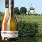 Zwei Weine von der Terra Alte Mühle, ein Roséwein und ein Weißwein, vor einem Weinberg mit Windmühle im Hintergrund. Probieren Sie herausragende Qualität!