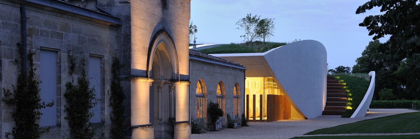 Historisches Weingut Chateau Cheval Blanc in Frankreich bei Abenddämmerung, zeigt beleuchtete Steinarchitektur und moderndes Gebäude im Hintergrund. Ein Juwel für Weinkenner.