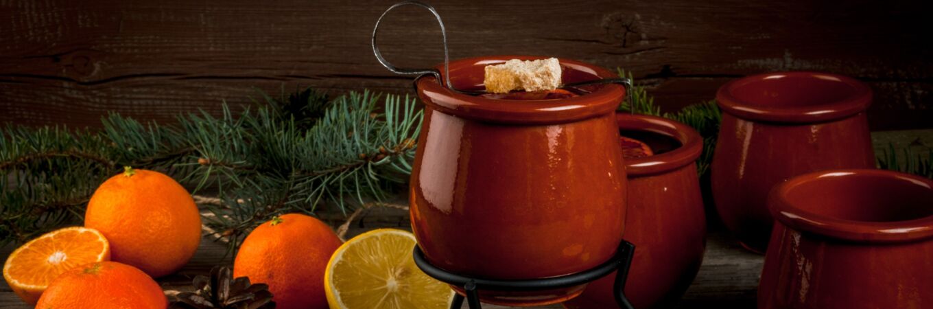 Orangene Feuerzangenbowle-Töpfe und Zutaten wie Orangen, Zimtstangen und Teelicht auf Holztisch. Perfekt für Weihnachtspartys.