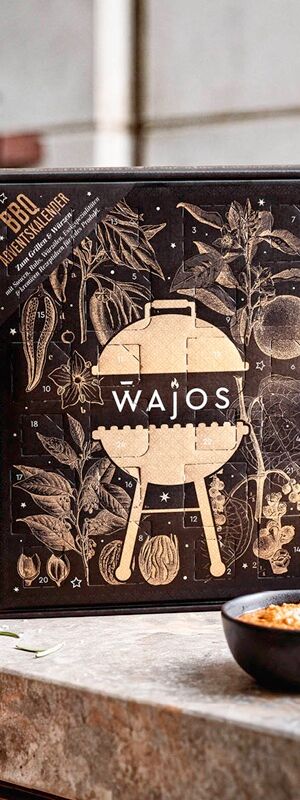Wajos Adventskalender BBQ 2026 in Schwarz und Gold mit 24 Türchen, weihnachtlichen Illustrationen von Grillzutaten, Gewürzen und Kräutern sowie zentralem Wajos-Logo.