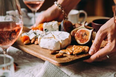 Zwei Gläser trockener Roséwein mit Käseplatte, Feigen und Crackern auf einem Holztisch, ideal für einen entspannten Abend.