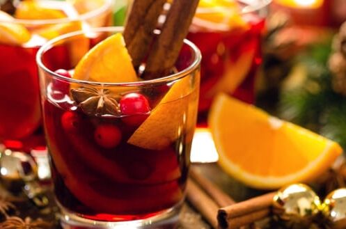 Glas Glühwein mit Zimtstange, Orangenscheiben und Beeren, dekoriert mit Tannen und Zapfen, weihnachtliche Atmosphäre.