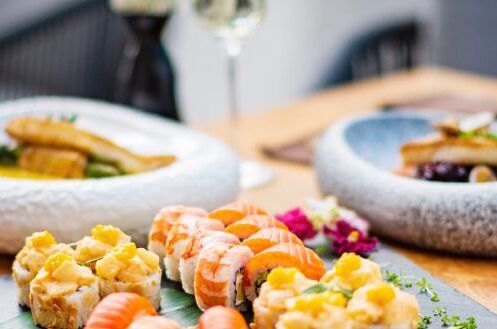 Eine Auswahl an Sushi-Gerichten auf einem Tisch, begleitet von einem Glas feinherbem Weißwein, ideal für ein stilvolles Dinner.