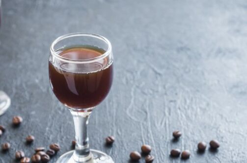 Zwei Gläser Kaffeelikör auf einem dunklen Tisch, umgeben von Kaffeebohnen. Der dunkle Likör glänzt im Licht. Perfekt für besondere Anlässe!