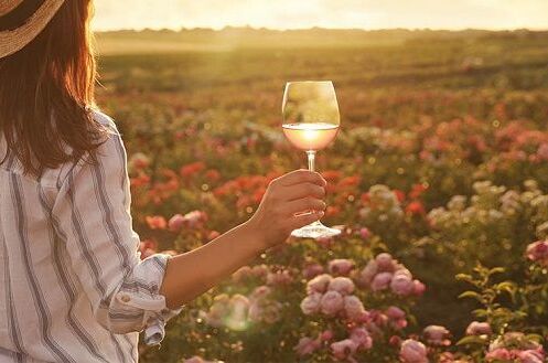 Eine Frau im Sommerkleid genießt ein Glas deutschen Roséwein im Sonnenuntergang vor einem blühenden Garten.