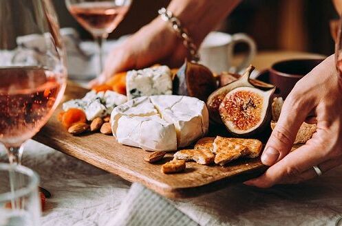 Zwei Gläser deutscher Roséwein neben einem Holzteller mit Käse, Feigen, Nüssen und Crackern. Perfekt für gesellige Abende!