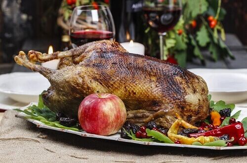 Festlicher Weihnachtsgänsebraten angerichtet mit frischen Kräutern und umgeben von buntem Gemüse, dazu Rotwein in Gläsern serviert.