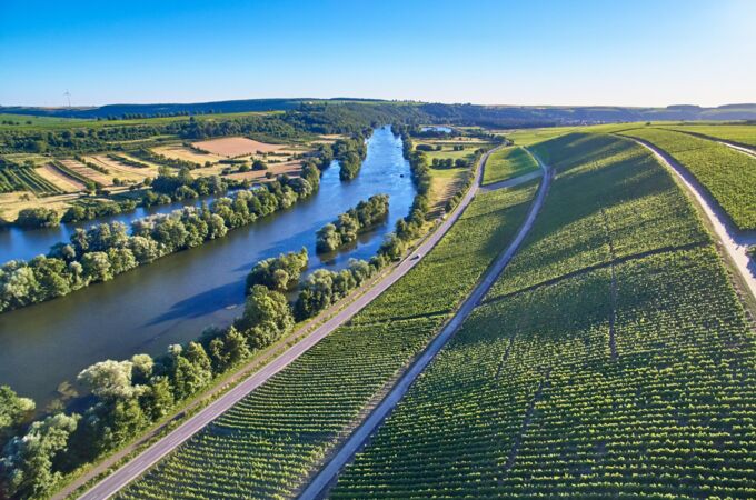 Luftaufnahme des Weinguts Zur Schwane in Deutschland mit üppigen Weinbergen entlang eines malerischen Flusses. Genießen Sie die traditionelle Weinbaukunst!