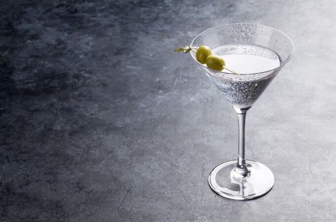 Martini-Glas mit Gin und zwei grünen Oliven auf einem grauen Tisch, ideal für stilvolles Gin-Genießen.