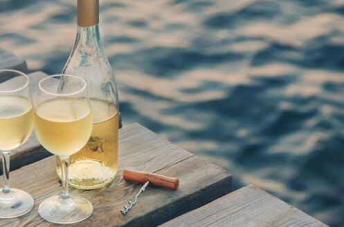 Zwei Gläser alkoholfreier Weißwein und eine geöffnete Weinflasche auf einem Holzsteg am Wasser. Entspannen und genießen Sie!